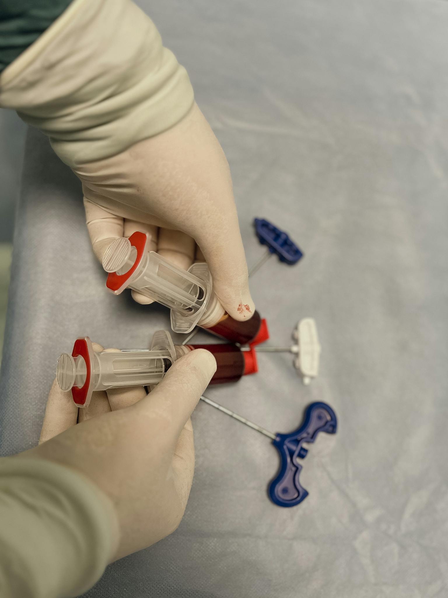 Gloved hands handling medical syringes and test tubes in a clinical setting.